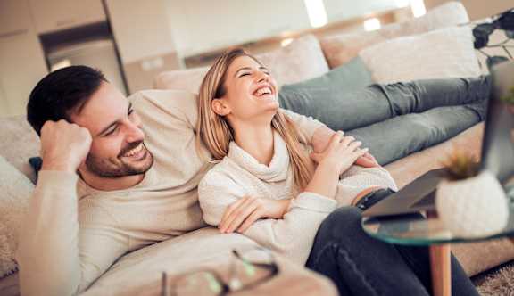 A man and woman are laughing together on a couch.