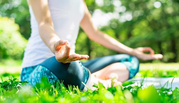 A person is sitting cross-legged on the grass in a meditative pose.
