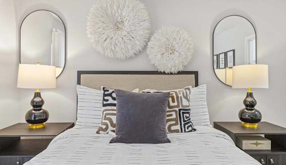 A bedroom with a bed, two lamps, and decorative pillows.