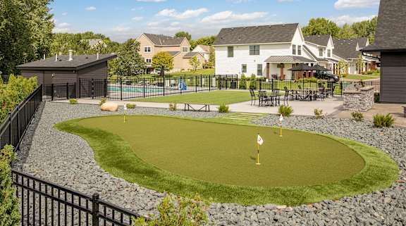 A golf hole is surrounded by a black fence and a green lawn.