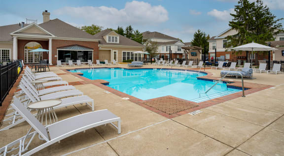 a large swimming pool with chairs and a building in the background