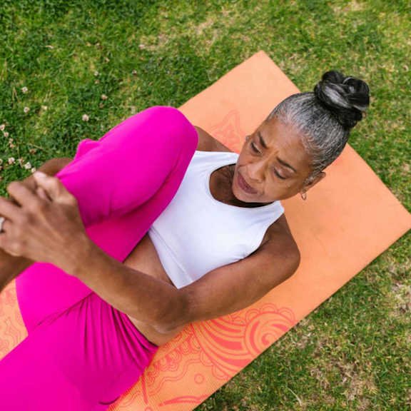 A woman in a pink dress is sitting on a yoga mat outdoors.