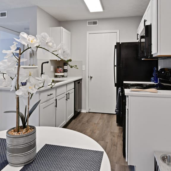 a kitchen with white cabinets and a black refrigerator and a table with a vase