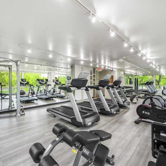A spacious fitness center at The Pavilion with a variety of equipment including treadmills, elliptical machines, and weight machines.
