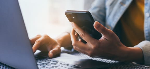 a person using a cell phone and a laptop computer