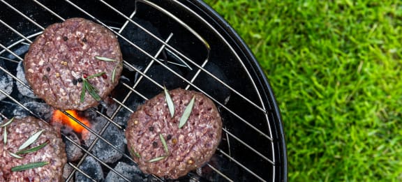 four burger patties cooking on a barbecue grill