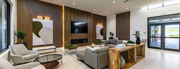 A modern living room with a large grey sofa, a wooden coffee table, and a flat-screen TV mounted on the wall.