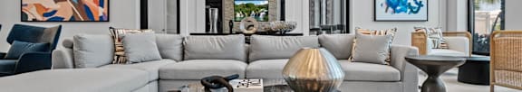 A modern living room with a grey sofa, a glass coffee table, and a large abstract painting on the wall at Altis Grand Twin Lakes, Kissimmee, FL 34744