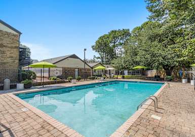 A swimming pool surrounded by a brick patio and trees at The Onyx Hoover Apartments, Hoover, AL, 35216