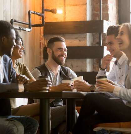 Friends Sitting Around Table Smiling and Laughing while Drinking Coffee