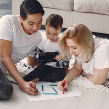 a family of three sits on the floor of their living room and draws on a piece of