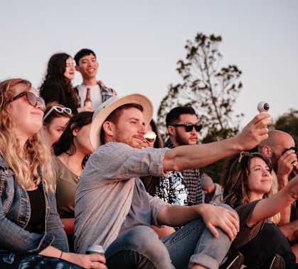 A group of people are sitting in a crowd, with one person taking a photo with a smartphone.