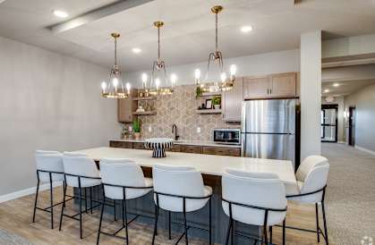 a kitchen with a large island with white chairs and a stainless steel refrigerator