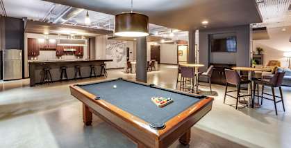 A pool table is in the middle of a room with a bar and a television.