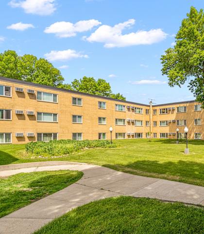 an exterior view of an apartment building with a green lawn and sidewalk