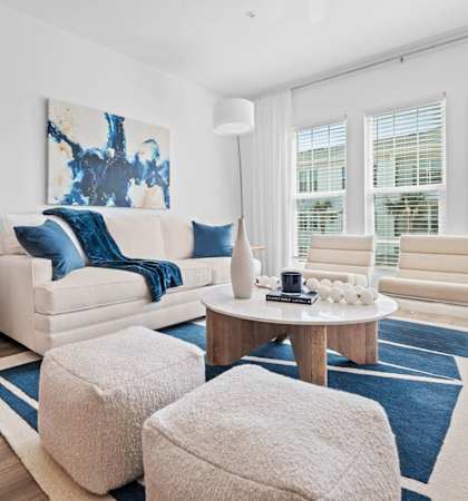 A living room with a white couch, a round table, and a large painting on the wall. at Altis Twin Lakes Apartments, Kissimmee, FL 34744