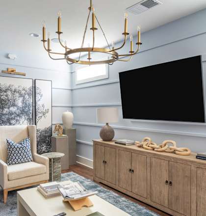 A living room with a white couch, a wooden coffee table, a chandelier, and a large flat screen TV mounted on the wall.