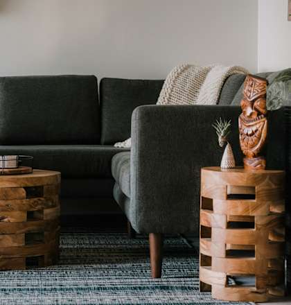 A living room with a grey couch, a wooden stool, and a wooden barrel.