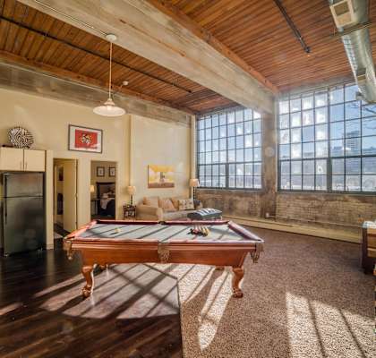 A billiard table is in the middle of a room with a wooden floor and a large window.