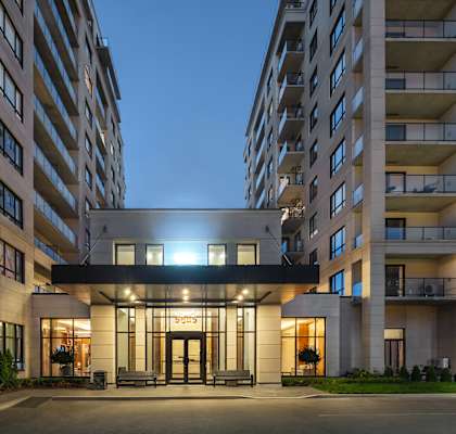 The image shows a modern building with a well-lit entrance and multiple balconies.