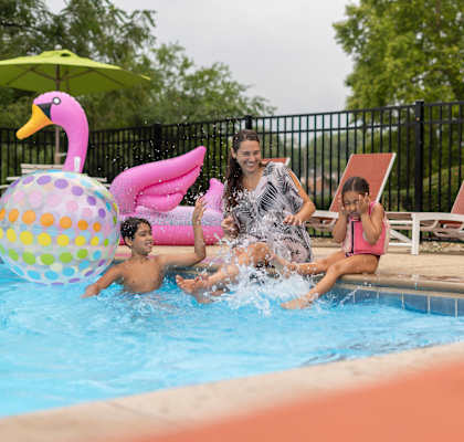 a woman and two children splashing in a swimming pool at The View Apartments St Charles, St Charles, 60174