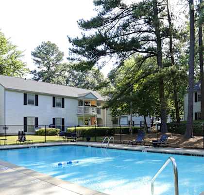 A swimming pool surrounded by trees and a white building.