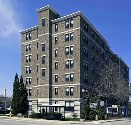 Seven story grey brick apartment building with trees.