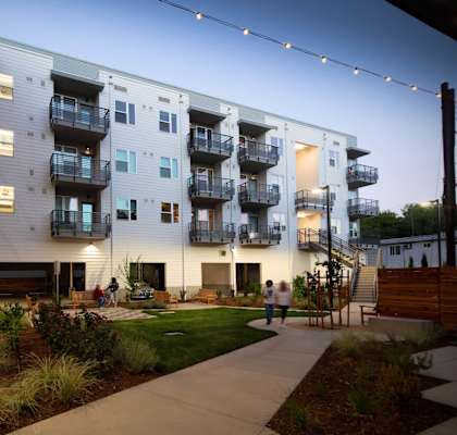 Interior courtyard at dusk with lighted balconies and walkways, showing green courtyard and walking path.