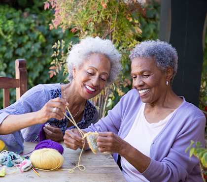 two women sitting at a table knitting together