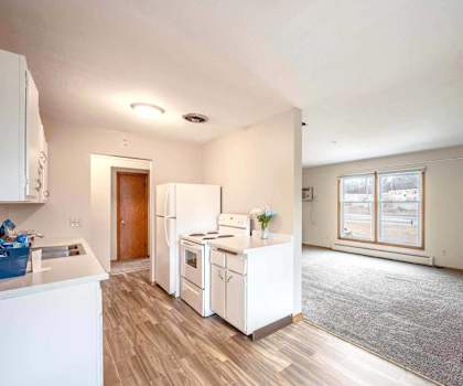 A kitchen with white appliances and a grey carpet.