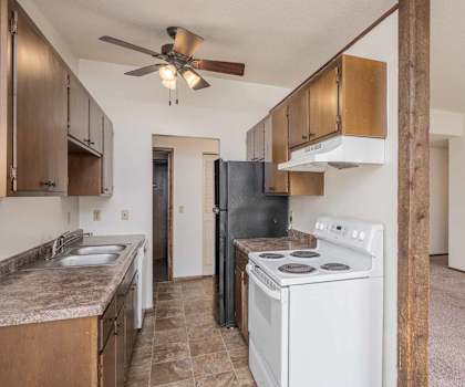 A kitchen with a black refrigerator, white stove, and wooden cabinets.