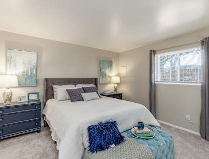A bedroom with a large bed, a nightstand with a lamp, and a window with curtains.