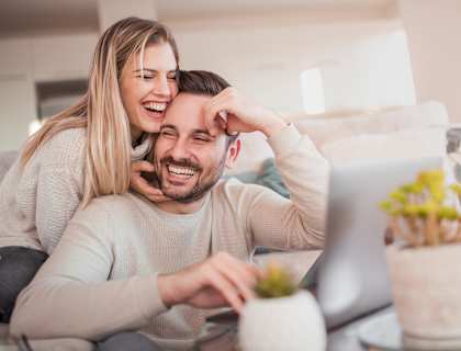 a man and a woman sitting on a couch looking at a laptop
