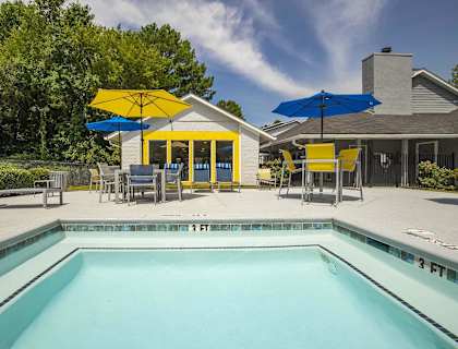A pool with a yellow umbrella and a house in the background.
