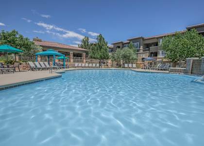 A large swimming pool with a blue umbrella and chairs.