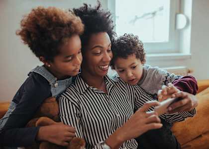 A woman and two children are sitting on a couch, looking at a smartphone.