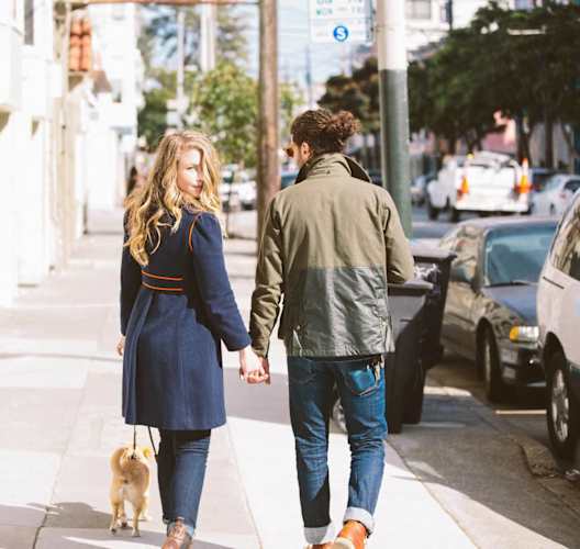 a man and woman walking a dog down a sidewalk