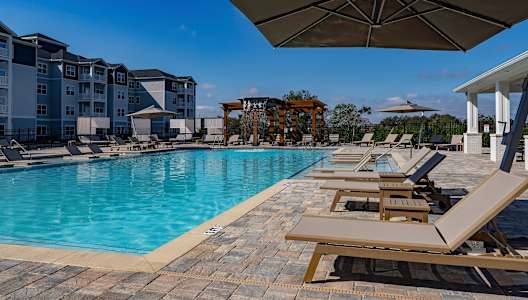 A pool with sun loungers and a building in the background.