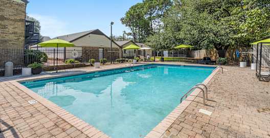 A swimming pool surrounded by a brick patio and trees.