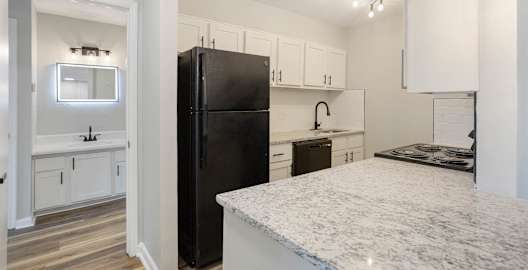 A black refrigerator stands in a kitchen with white cabinets and a marble countertop.