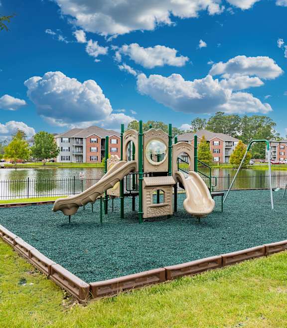 A playground with a green slide and a brown swing set.