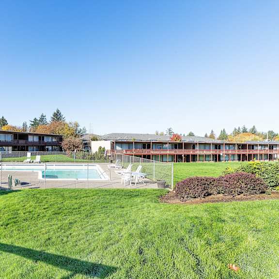 A large grassy area in front of a building with a pool table and chairs.