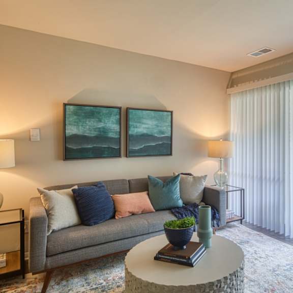 A living room with a grey couch, a round table, and two framed pictures on the wall.