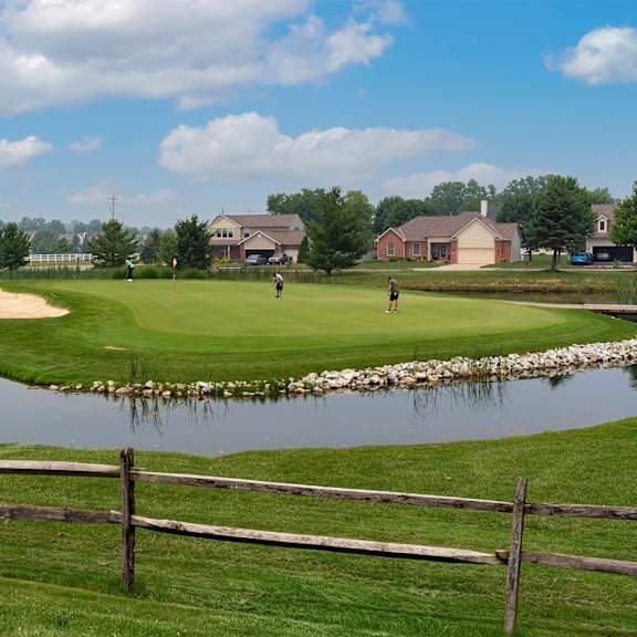 A golf course with a pond and a fence.