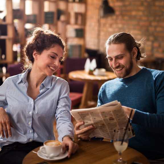 two people sitting at a table in a cafe drinking coffee