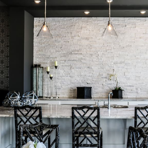 A kitchen with a white brick wall and black chairs.