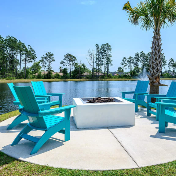 a patio with blue chairs and a fire pit near a lake
