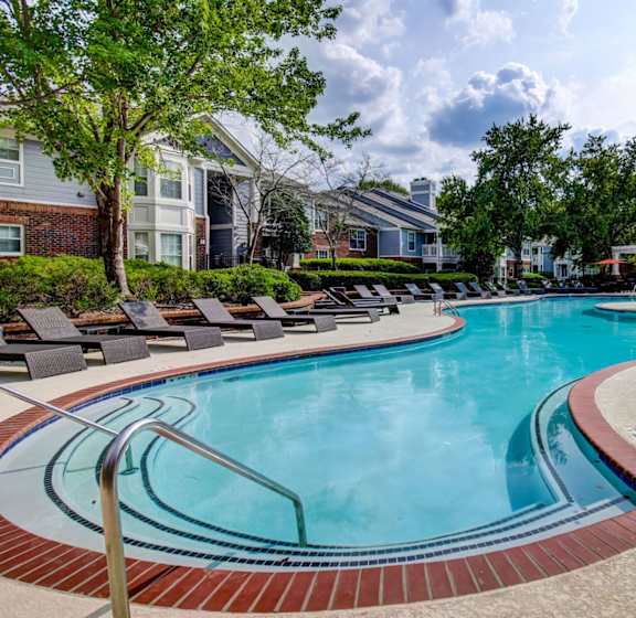 A swimming pool surrounded by a brick border and lounge chairs.