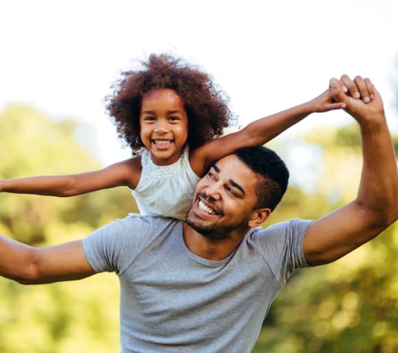 a father holding his daughter on his shoulders while playing in the park at Brightwaters Apartments, Little Rock, Arkansas
