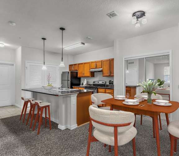 a dining area with a table and chairs and a kitchen in the background